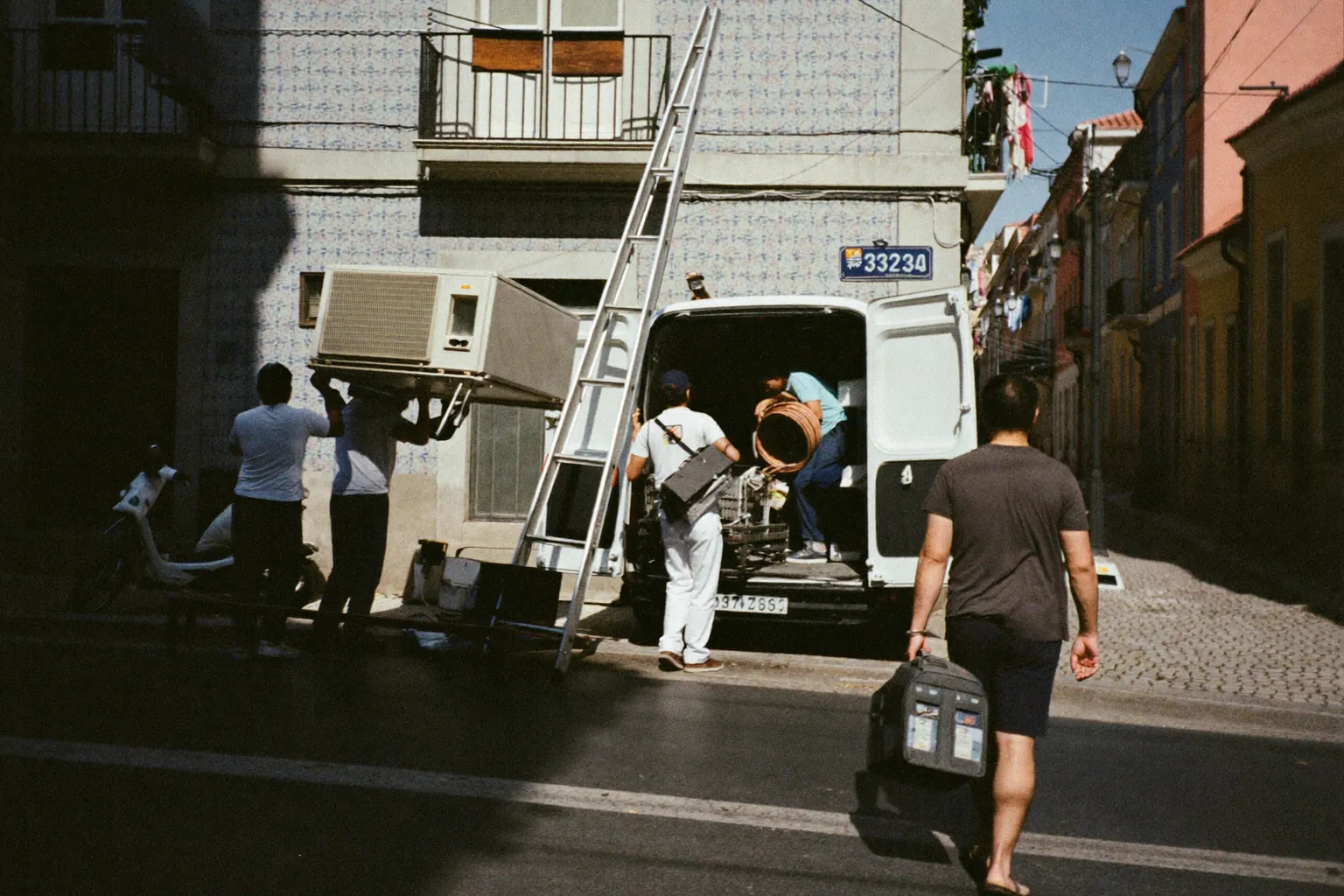 Installers unloading an air-conditioning unit from a van on a Lisbon street